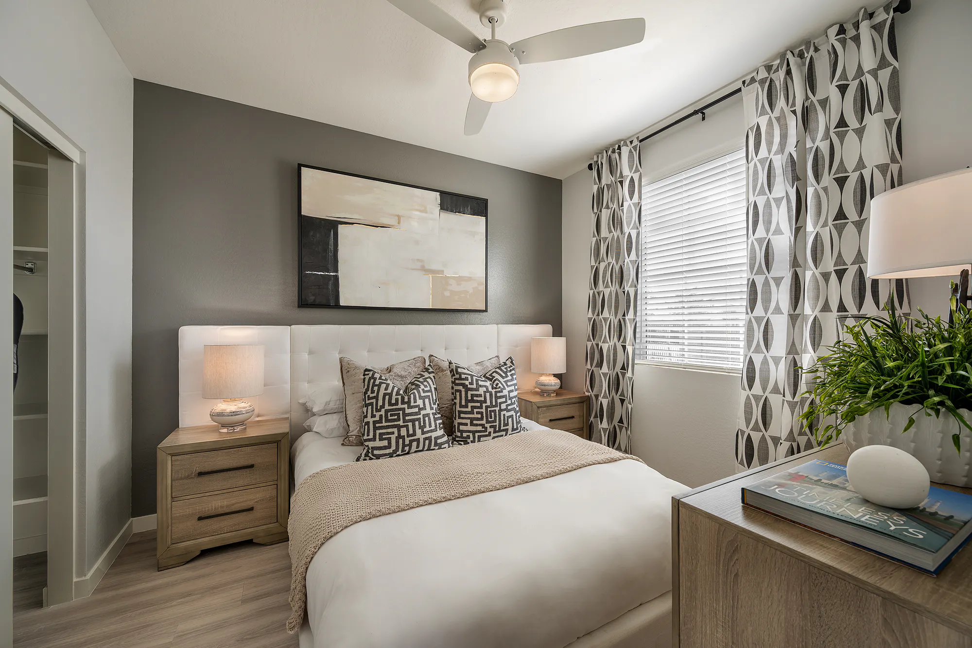 Furnished bedroom with a ceiling fan and patterned curtains.